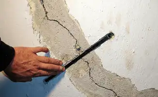 A wall with a large crack is being inspected by a professional in Spokane, WA